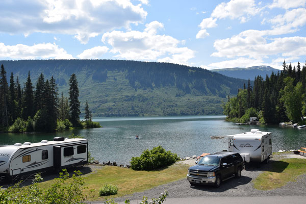 RVs parked at campground on shores of a lake surrounded by spruce forest