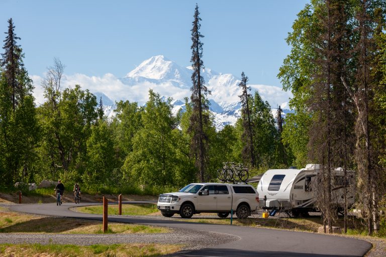 SUV towing a camper in a campground with views of Denali