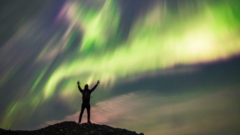 See the Northern Lights in Alaska A man stands silhouetted against aurora display
