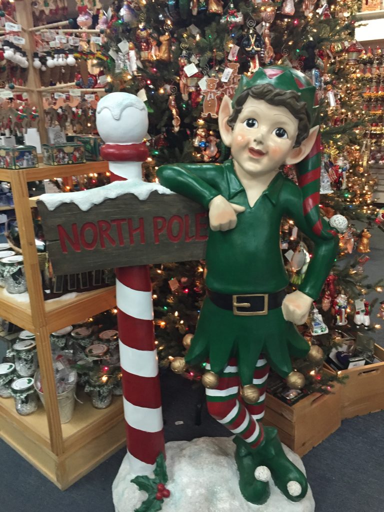 fake elf leaning on a North Pole candy cane striped pole by Christmas decorations