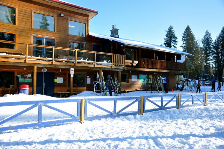 A wooden ski lodge with snow on the roof and ground out front