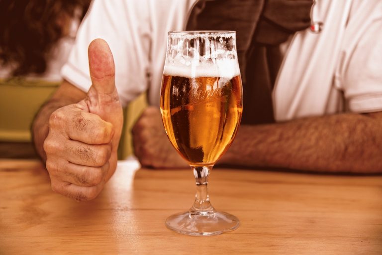 A Belgian beer glass with partially finished beer and a guy giving thumbs up