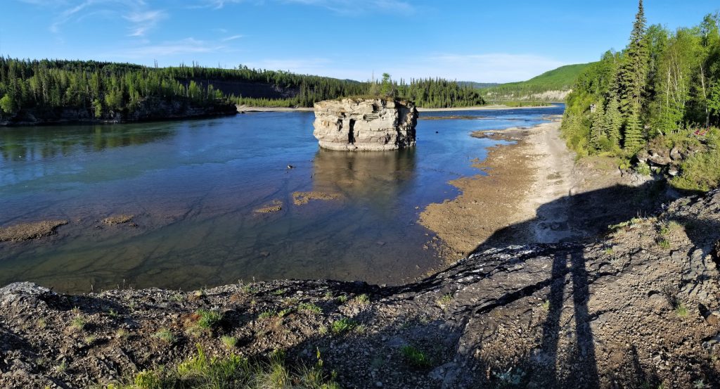 A calm river passes through wilderness. One large rock outcropping has a tree growing on top