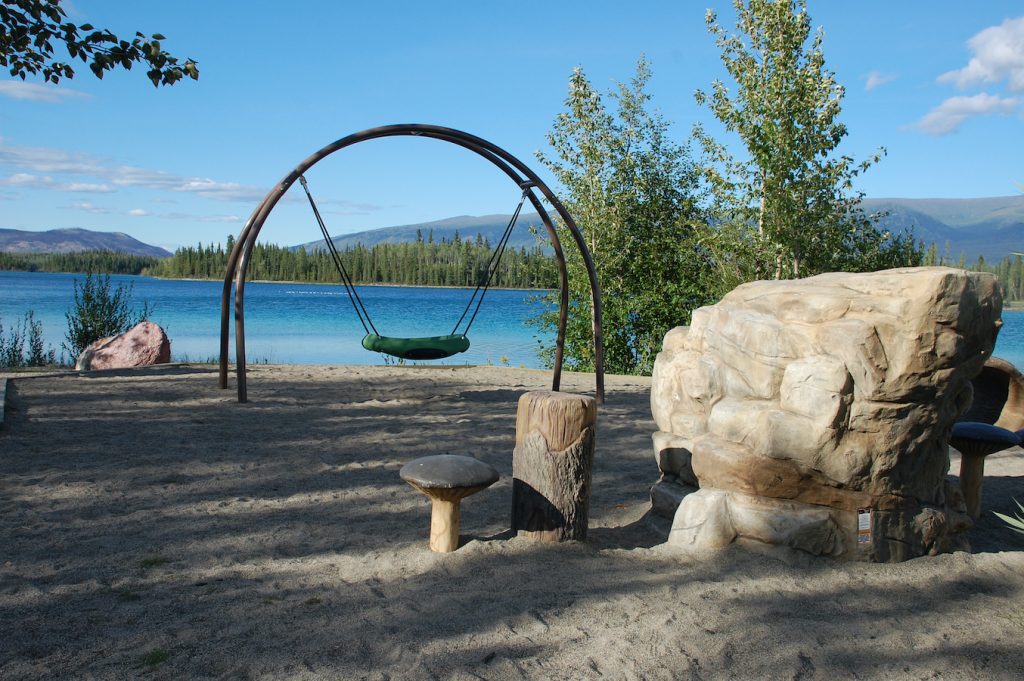 Sandy beach, big rock, and hanging chair along the shores of a beautiful blue lake