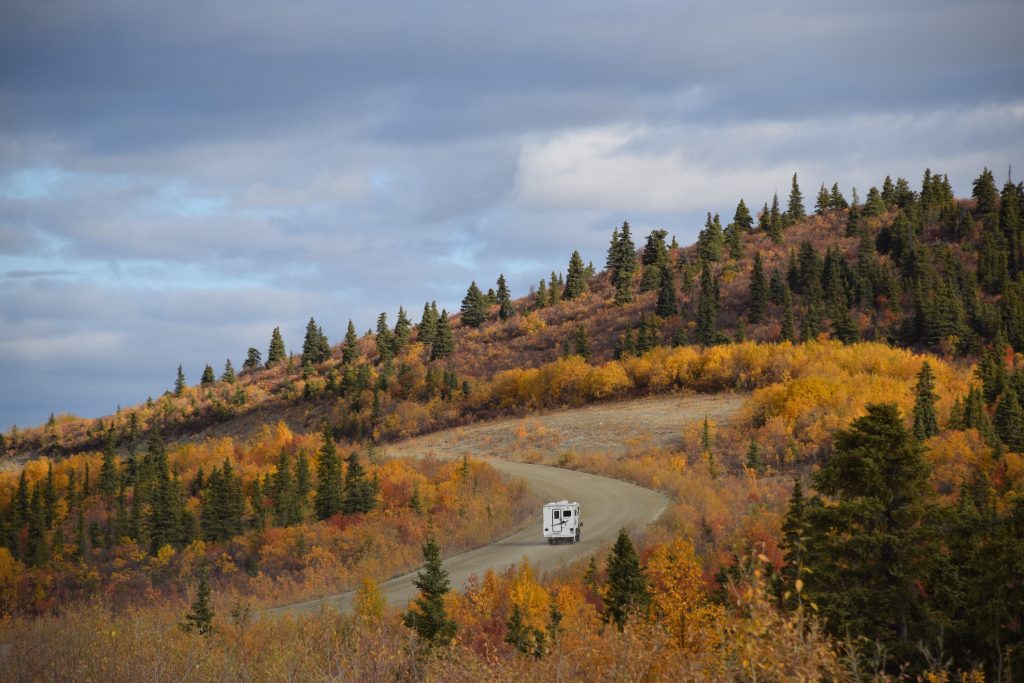 Motorhome wends around curve in a road through yellow and green trees