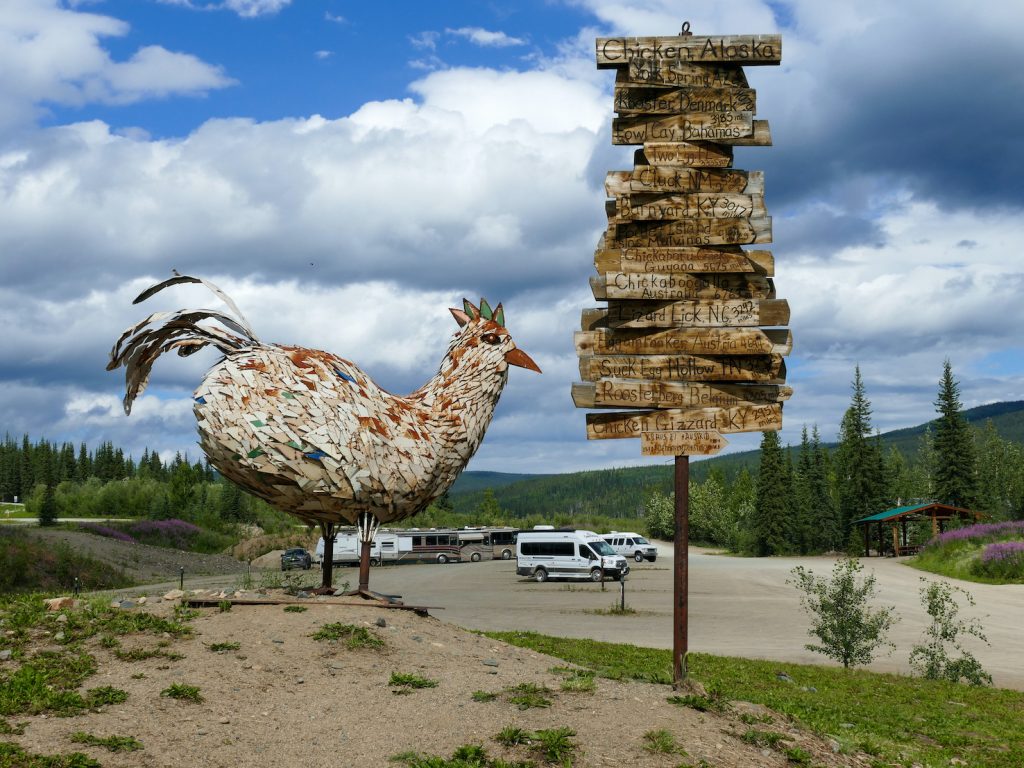 A giant sculpture of chicken made out of old lockers and a sign pointing to destinations with distances